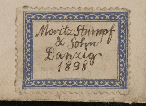 Jedna z kart we wnętrzu albumu Czarnych Huzarów. Na fragmencie karty karteczka w kształcie znaczka z odręcznym napisem "Moritz Stumpf, niżej "& Sohn", niżej "Danzig" i niżej data "1898". 