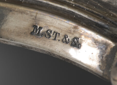 Zdjęcie przedstawia srebrny element z wybitą inskrypcją "M. ST. & S" od Mortiz Stumpf & Sohn (Maurycy Stumpf i Syn)