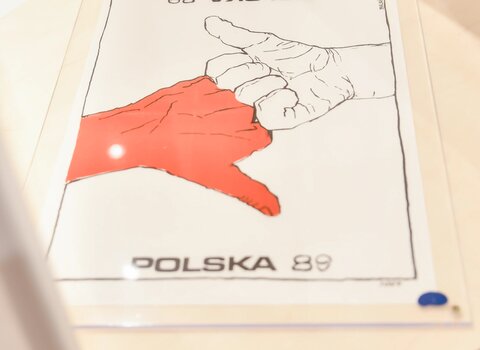 Plakat wyborczy przedstawia dwie dłonie z kciukiem w górę. Dłonie stykają się palcami. Jedna jest biała druga czerwona. Z góry i dołu napis Polska'89