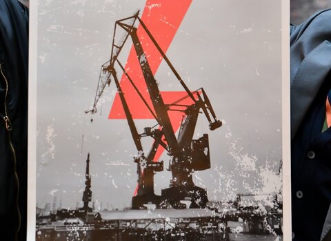Przekazany przez Michała Marcinkowskiego plakat. Na nim żuraw portowy zakrywający fragmenty dominującego nad nim pioruna. Poniżej hasło „Gdańsk to dźwignie”. Plakat trzymają dwie pary dłoni.   

