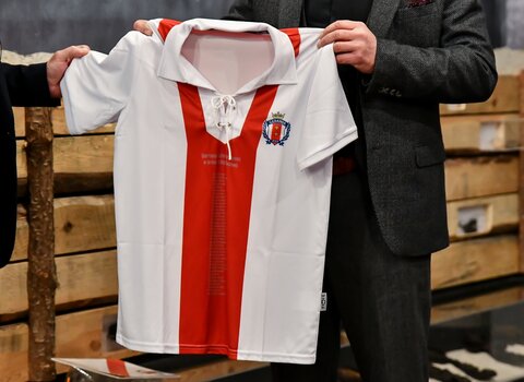 Na zdjęciu okolicznościowa koszulka piłkarska GKS Gedania 1922. W środku koszulki podłużny czerwony pas, boki i rękawy są białe.  