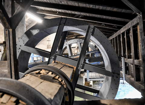 Zdjęcie. Wnętrze Kuźni Wodnej w Oliwie. Na pierwszym planie odnowione koło wodne otoczone stalową obejmą. 