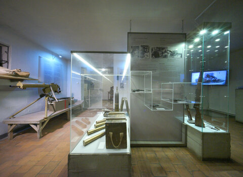 Zdjęcie przedstawia salę wystawową we wnętrzu Wartowni. Widoczne szklane gabloty z uzbrojeniem używanym przez żołnierzy Wojskowej Składnicy Tranzytowej oraz tablice informacyjne na ścianach. 