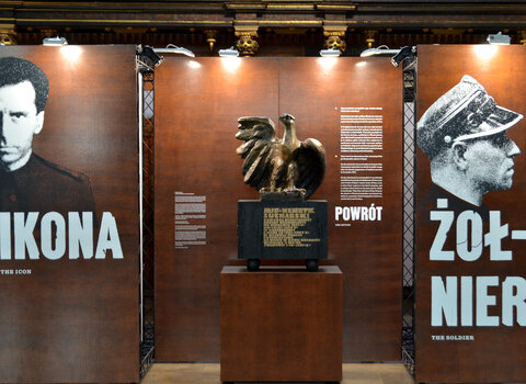 Fragment wystawy. Pośrodku stoi posąg orła bez korony. Po jego obu stronach plansze ze zdjęciami i napisami. Po lewej Ikona, po prawej Żołnierz.