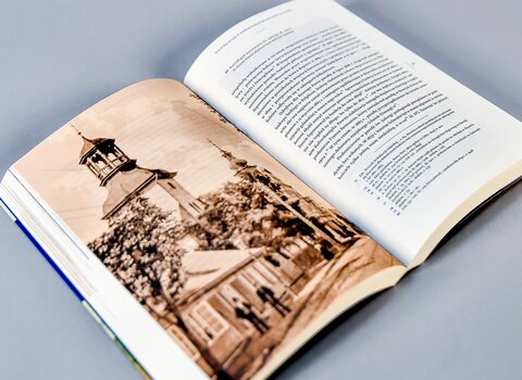 Zdjęcie. Otwarta książka. Na lewej stronie fotografia kościoła w sepii. Na prawej stronie tekst.  