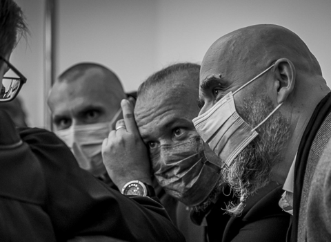Zdjęcie czarno-białe. Trzech mężczyzn rozmawia z prawnikiem na sali rozpraw. Zbliżenie na twarze. 