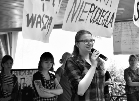 Zdjęcie czarno-białe. Gdański protest akademicki w 2018 roku. Na scenie przemawiają studentki. Nad nimi 3 transparenty z napisami "Za naukę naszą i waszą", "Strajk studencki" oraz "#naukaniepodległa". 