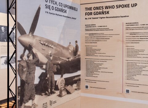 Plansza wstępna wystawy, przedstawia mechaników naprawiających myśliwiec. 