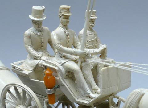 Zdjęcie przedstawia białą dorożkę z trzema jadącymi na niej mężczyznami. 