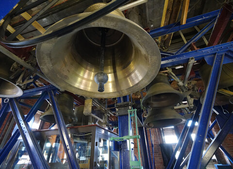 Zdjęcie wykonane w wieży kościoła św. Katarzyny (Muzeum Nauki Gdańskiej). Widok na zespół dzwonów – carillon, zawieszony na stalowej konstrukcji. Na pierwszym planie widoczny od dołu dzwon. W dali widoczne cztery dzwony oraz przeszklone niewielkie pomieszczenie, w którym gra carillonista. 