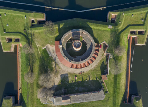 Zdjęcie Twierdzy Wisłoujście wykonane z drona. Ujęcie przedstawia Twierdzę z góry centralnie nad wieżą. Widać również bastiony oraz wodę otaczającą budowlę. 