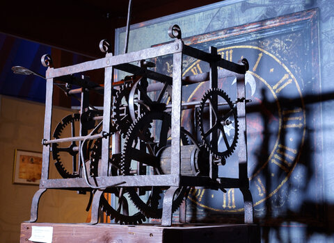 Zdjęcie przedstawia mechanizm starego zegara wieżowego. Konstrukcja szkieletowa, w środku koła zębate i przekładki.