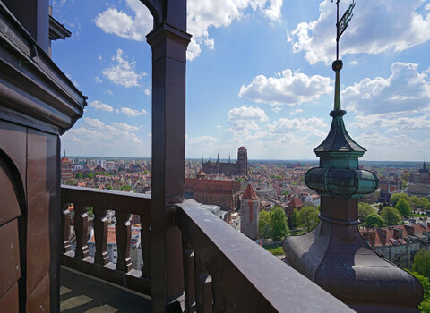 Zdjęcie panoramy Gdańska widocznej z wieży widokowej kościoła św. Katarzyny. Na pierwszym planie balustrada otaczająca punkt widokowy, w tle zabudowania Głównego Miasta z sylwetką Bazyliki Mariackiej. 