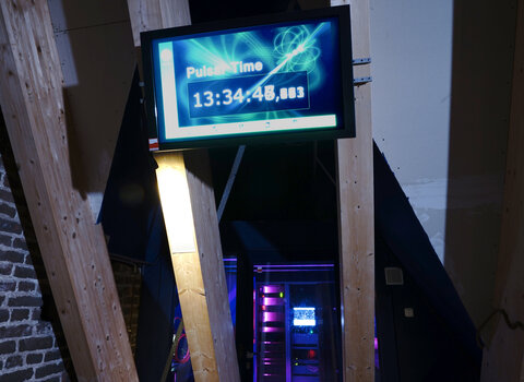 Zdjęcie przedstawia wnętrze sali wystawowej. Na pierwszym planie ekran z zegarem pulsarowym odmierzającym czas. 