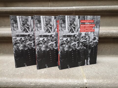 Zdjęcie przedstawia trzy książki stojące na kamiennych schodach. Na okładce książki w odcieniach szarości widniej Adolf Hitler w otoczeniu niemieckich oficerów. Na okładce czerwone prostokąty z tytułem książki i imieniem oraz nazwiskiem autora.