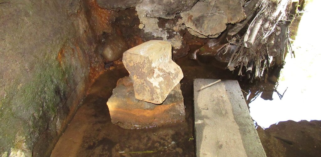 Zdjęcie przedstawia uszkodzony fragment kowadła leżący na kamieniu. Wokół płytka woda.