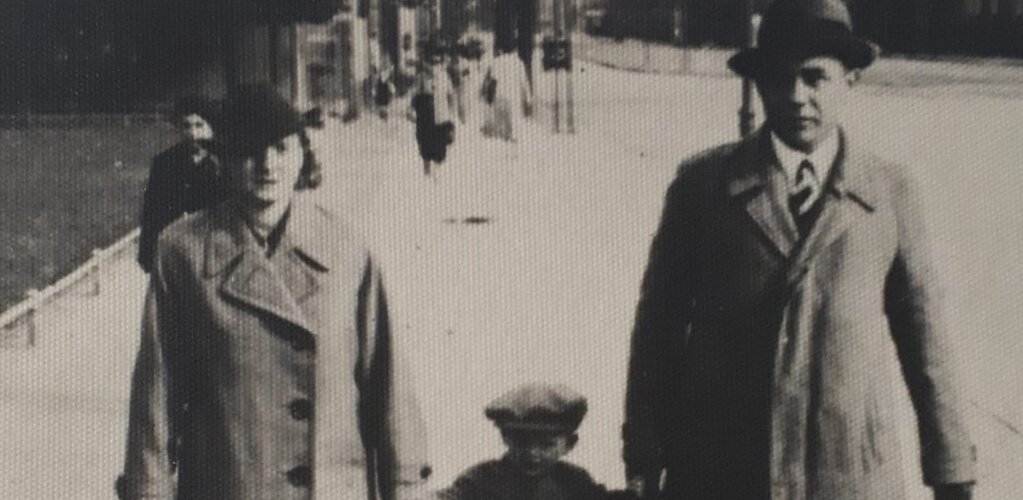 Brunon Bronk z żoną Klarą na spacerze trzymają za ręce syna Jerzym. W tle ulica i spacerujący ludzie.  