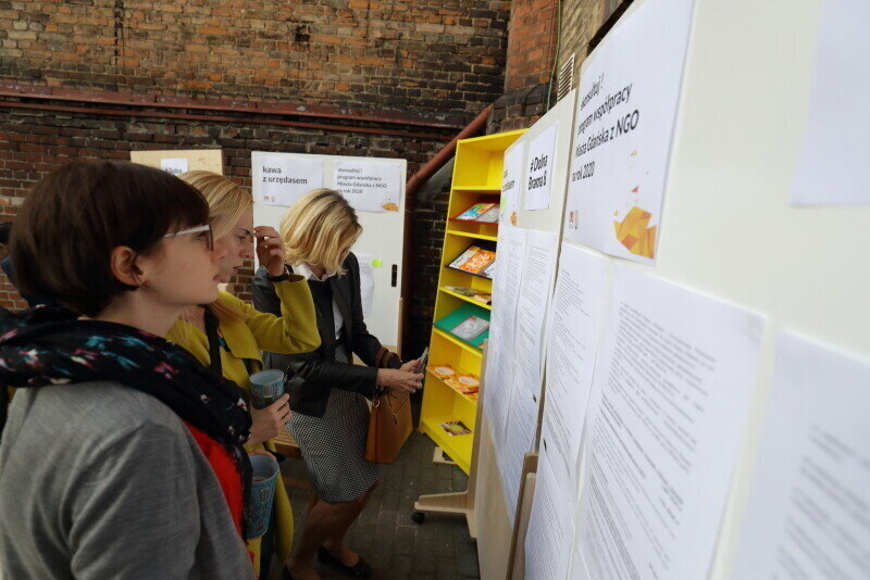 Zdjęcie z wydarzenia dla organizacji pozarządowych. Na fotografii trzy osoby czytają informacje z tablicy ogłoszeń.