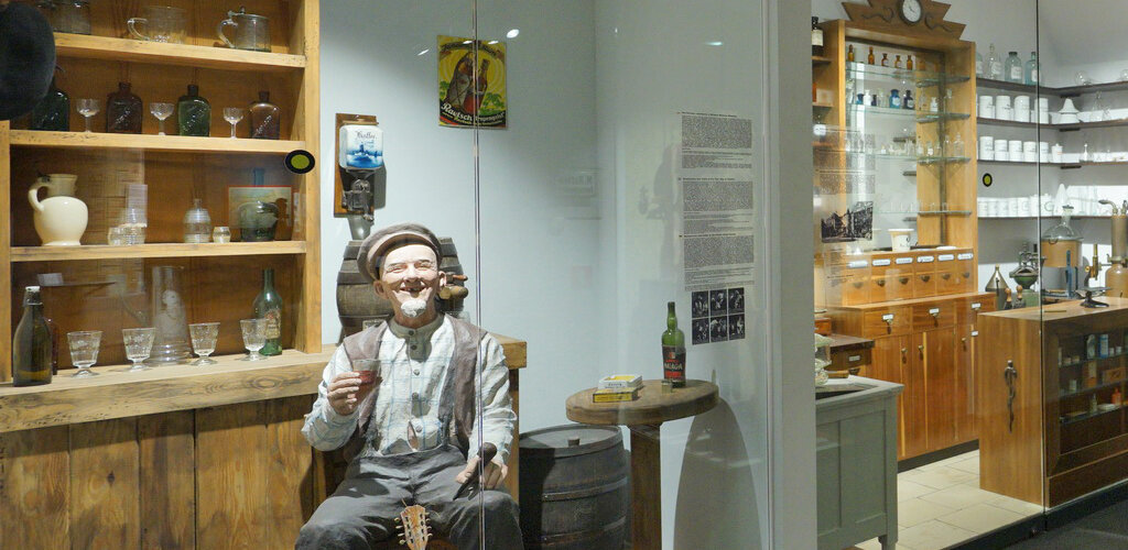Zdjęcie przedstawia salę wystawową, szklane galerie sklepów oraz odtworzone pomieszczenia mieszkalne z okresu Wolnego Miasta. Z jednej na widza spogląda uśmiechnięty sędziwy gdański bówka. 