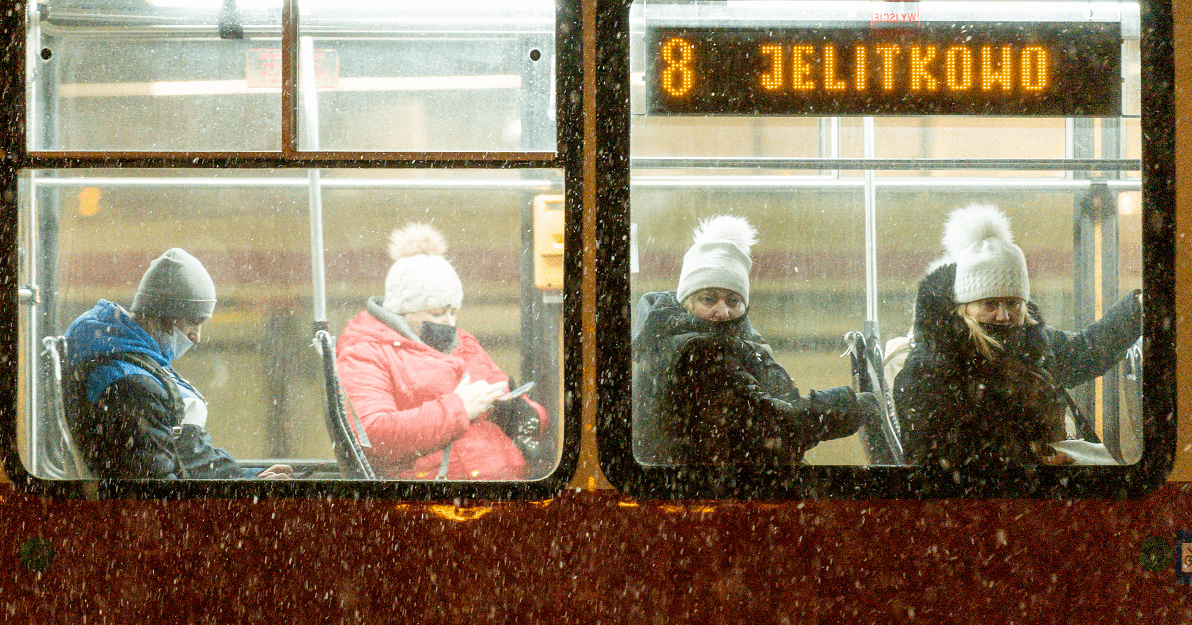 Zdjęcie. Fragment tramwaju z dwoma oknami. Wewnątrz siedzą 4 osoby z maseczkami zakrywającymi częściowo twarz. Patrzą  w telefon, albo w szybę (w kierunki widza). W prawym oknie u góry napis "8 Jelitkowo". Pada śnieg.   